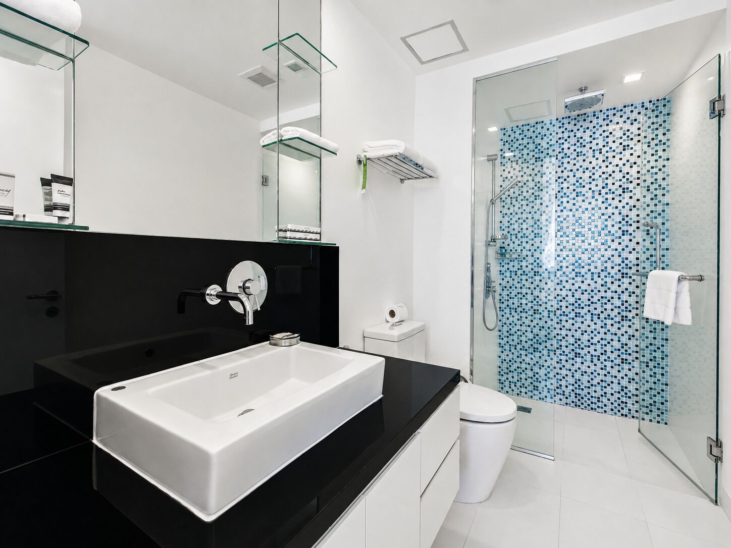 Un baño moderno con un lavamanos grande de color blanco, cabina de ducha de vidrio y encimera negra.