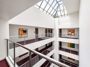 Un interior de varios niveles con barandillas de cristal y obras de arte en las paredes.