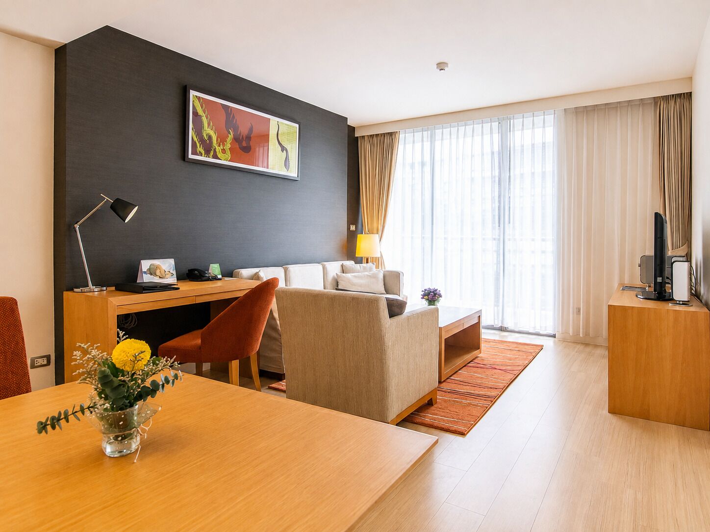 Ein modernes Hotelzimmer mit Schreibtisch, einer Couch, einem Esstisch und einem großen Fenster mit Vorhängen.