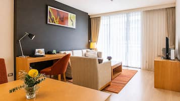 Ein modernes Hotelzimmer mit Schreibtisch, einer Couch, einem Esstisch und einem großen Fenster mit Vorhängen.