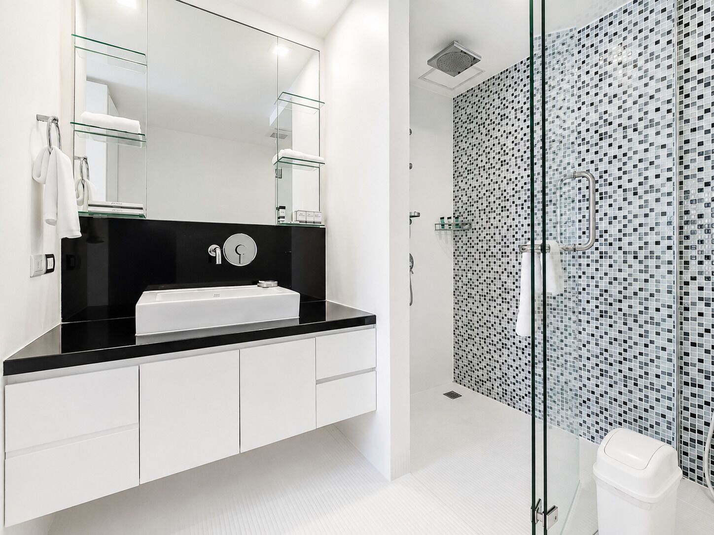 A modern bathroom with a black countertop, white cabinets, a glass shower enclosure, and a tiled shower wall.