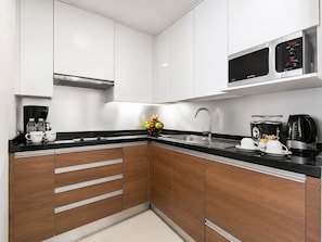 A modern kitchen with white cabinets, a black countertop, stainless steel appliances, and a microwave above the sink. - Oakwood Residence Sukhumvit 24 Bangkok (Bangkok)