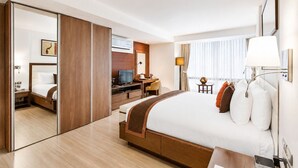 A hotel room with a large bed, a desk with a computer, a TV, and a mirror.