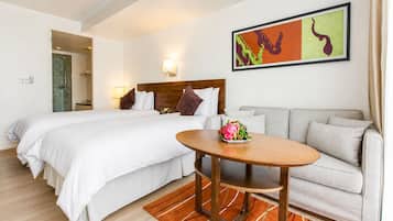 A hotel room with a bed, a sofa, a table with fruit, a painting, and a shower area.