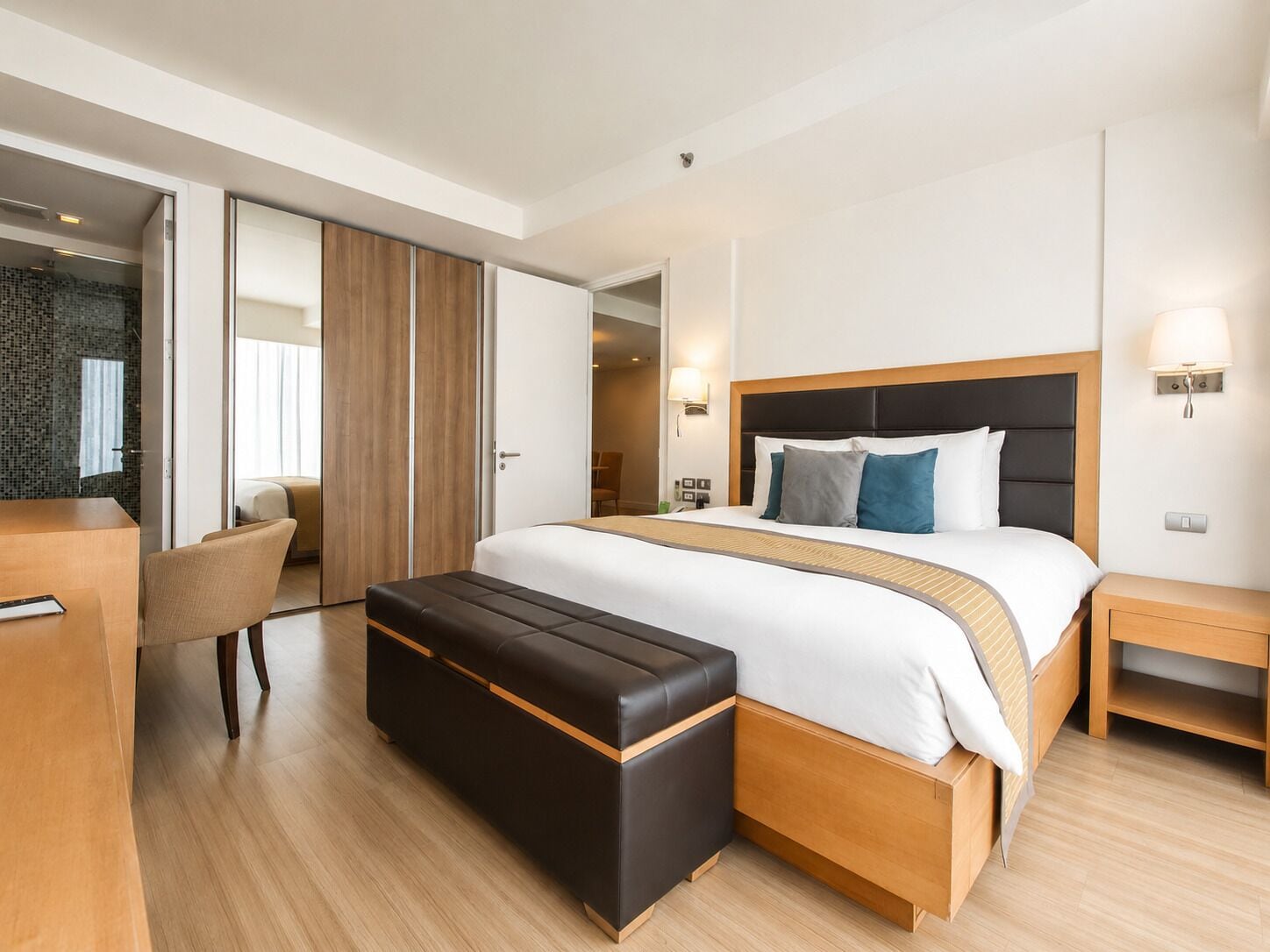 A modern hotel room with a large bed, a wooden bench, a desk, and a chair.