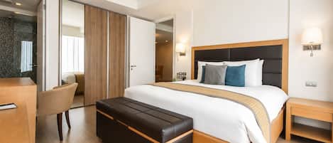 Una habitación de hotel moderna con una cama grande, un banco de madera, un escritorio y una silla.