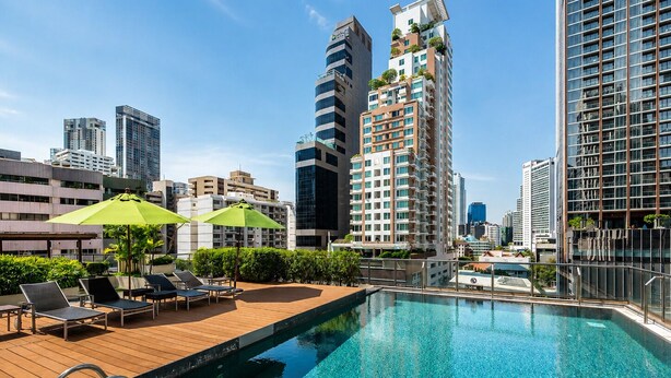 A rooftop pool with lounge chairs and umbrellas, surrounded by high-rise buildings.