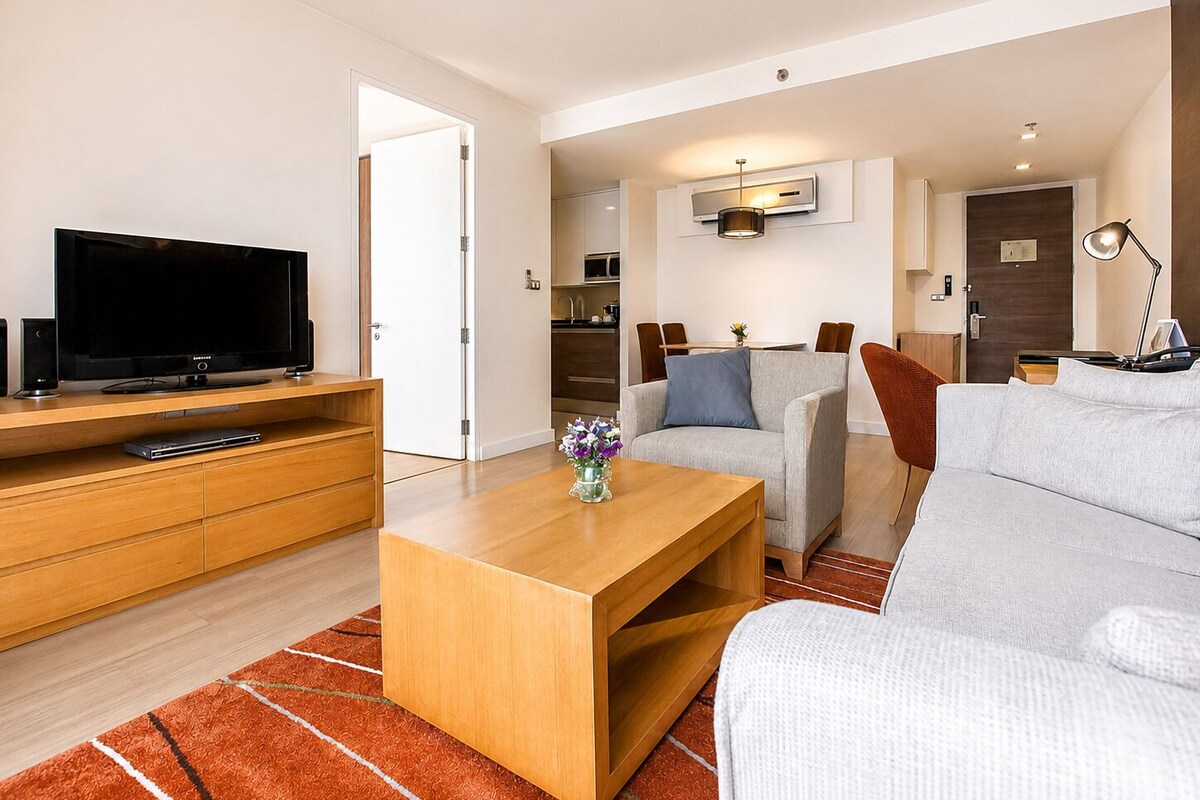 Una sala de estar moderna con televisor de pantalla plana, mueble de entretenimiento de madera, sofá gris y una mesa de centro.