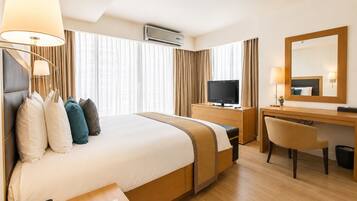 A hotel room with a large bed, a desk with a television, a chair, and a desk lamp.