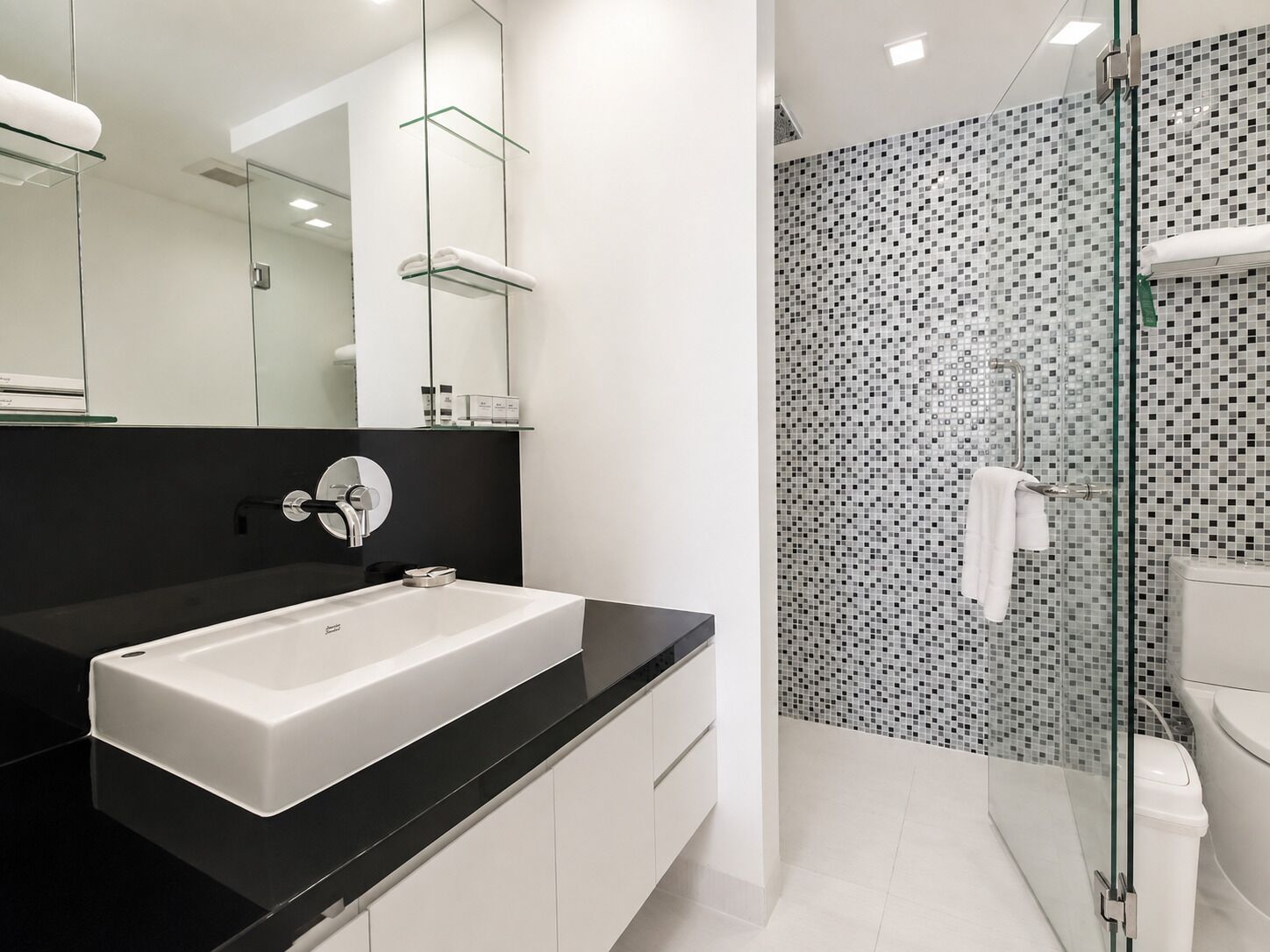 A modern bathroom with a white sink, black countertop, and a shower with mosaic tiles.