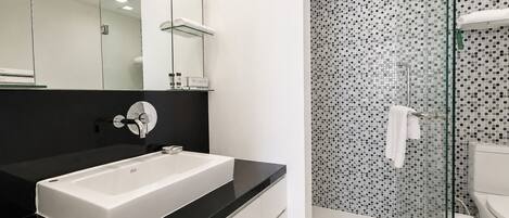 A modern bathroom with a white sink, black countertop, and a shower with mosaic tiles.