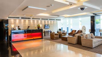 A modern hotel lobby with a reception desk, seating area, and large windows.