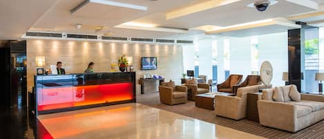 A modern hotel lobby with a reception desk, seating area, and large windows.