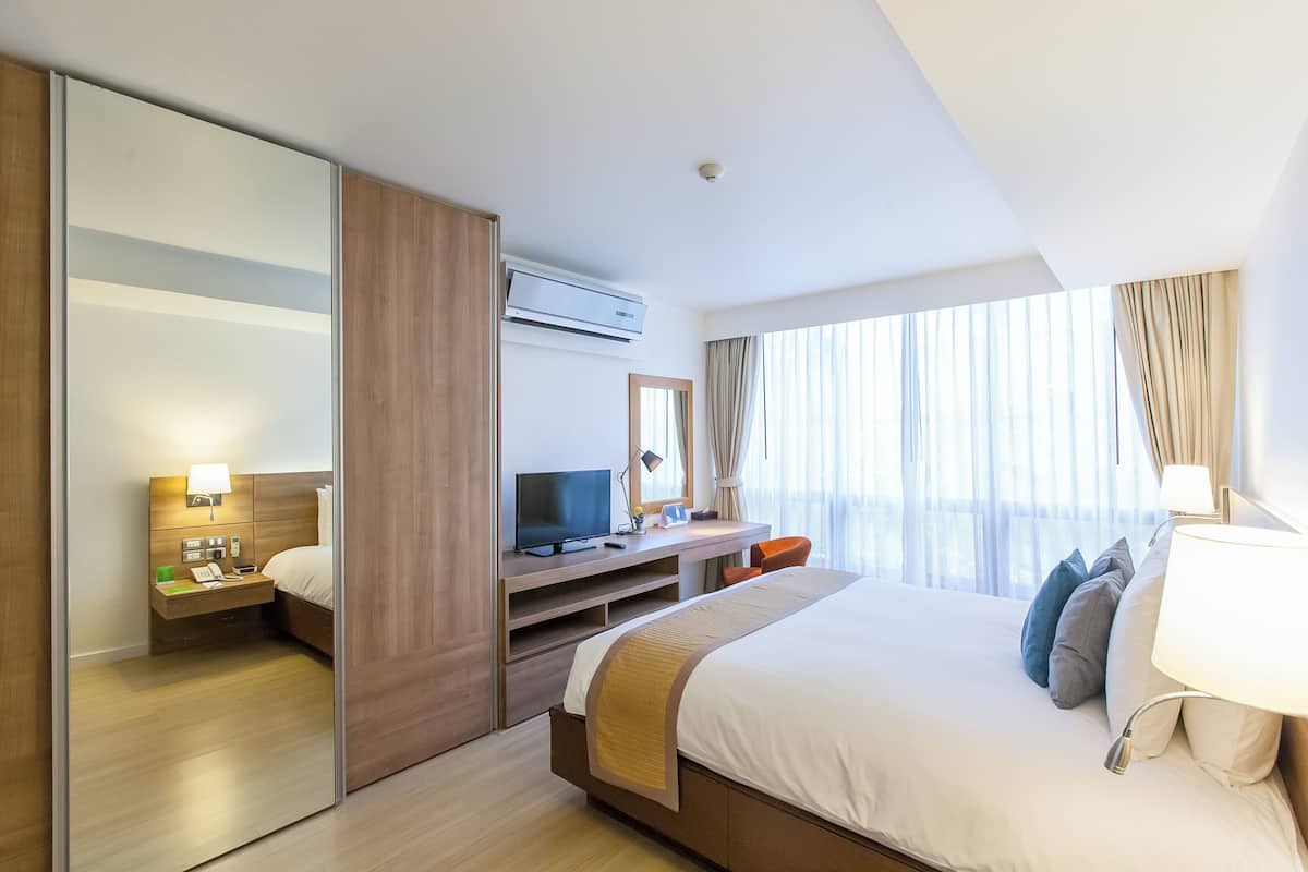 A hotel room with a bed, a desk, a TV, a mirror, and a window with curtains.