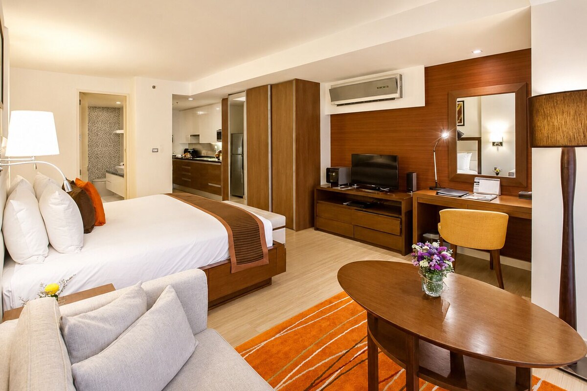 Una habitación de hotel con cama, escritorio, televisor, ordenador portátil, silla y mesa de comedor.