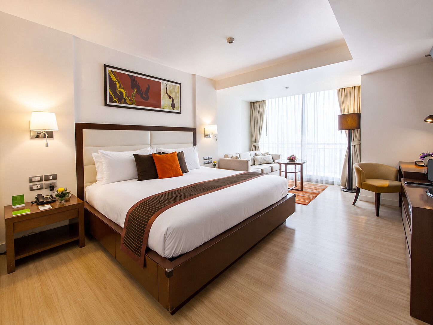 A hotel room with a large bed, a desk, a chair, a sofa, and a painting on the wall.