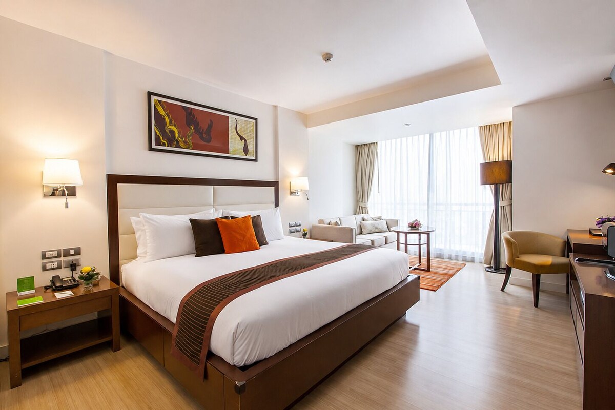 Una habitación de hotel con una cama grande, un escritorio, una silla, un sofá y un cuadro en la pared.