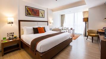 A hotel room with a large bed, a desk, a chair, a sofa, and a painting on the wall.