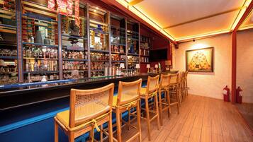 A bar area with multiple shelves of bottles, a television mounted on the wall, and several wooden bar stools.