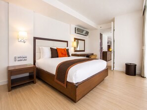 Una habitación de hotel con una cama grande, mesitas de noche, un escritorio y un cesto de basura.