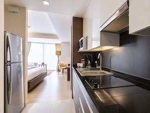 A modern hotel room with a kitchenette, a bed, a sitting area, and a view of the city.