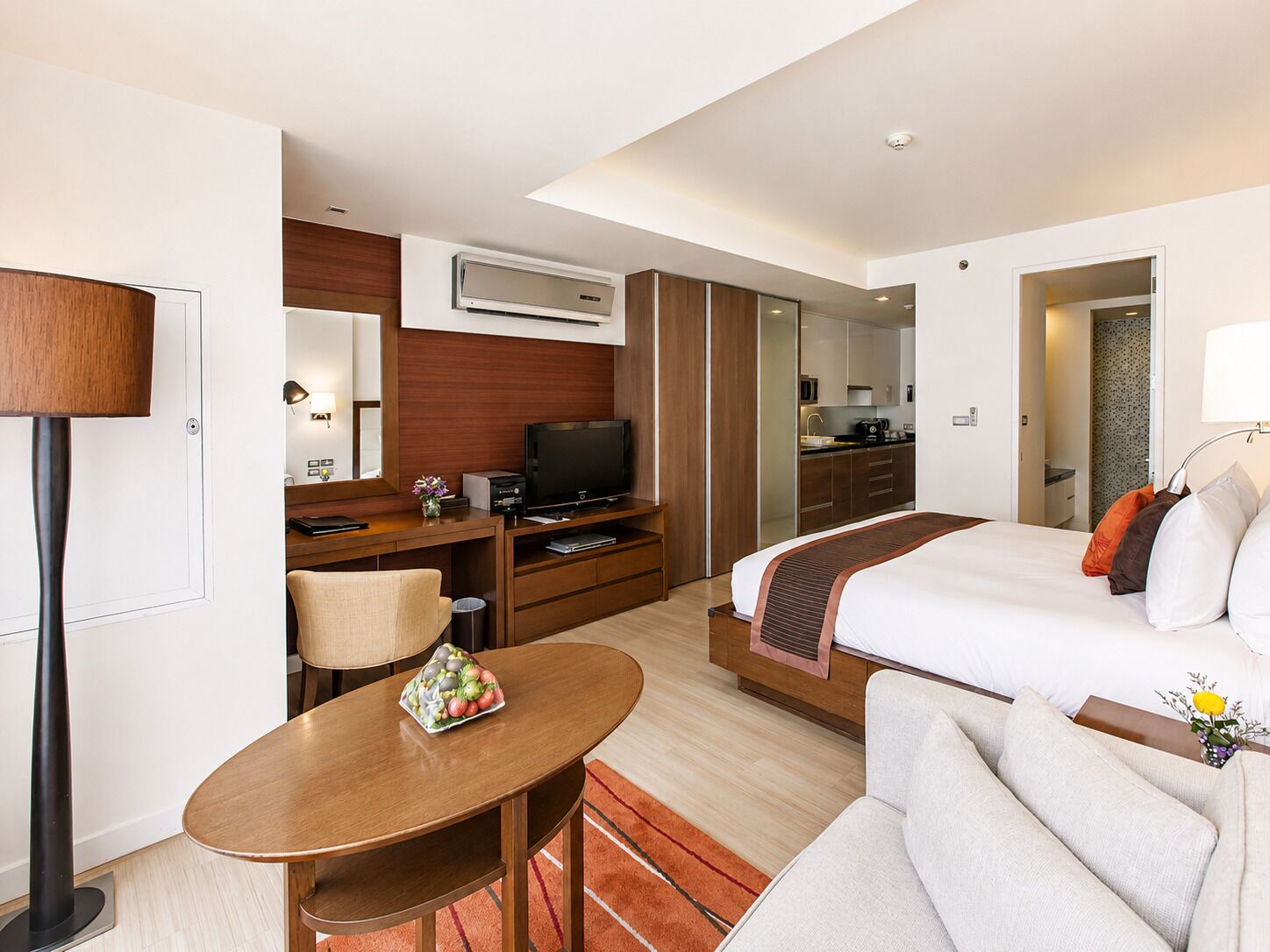 A hotel room with a bed, a desk, a television, a mirror, and a kitchenette.