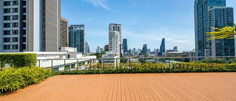A rooftop terrace with a view of a city skyline, featuring modern buildings and a clear sky.