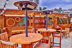 An outdoor wooden deck with round tables and chairs, string lights, and a neon sign. - Coachman Hotel (Glasgow)
