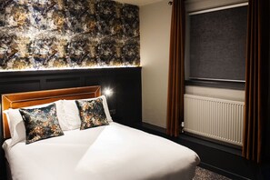 A hotel room with a large bed, a headboard with a light fixture, a wall with a textured pattern, and a window with curtains. - Coachman Hotel (Glasgow)