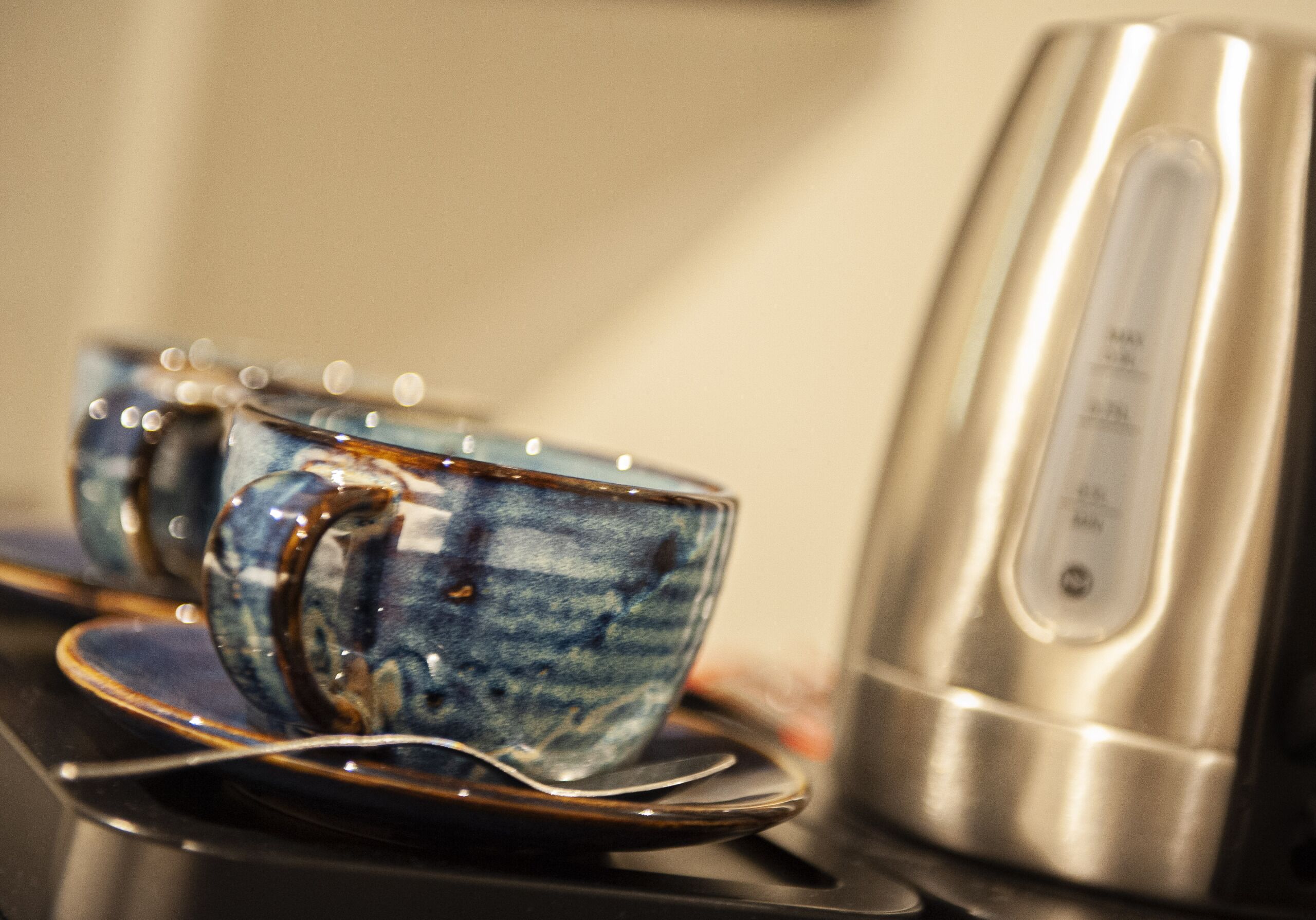 Un juego de tazas de cerámica sobre una bandeja, junto a una tetera eléctrica de acero inoxidable.
