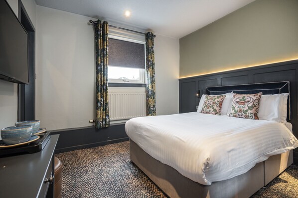 Habitación de hotel con una cama grande, un aparador y una ventana con cortinas.