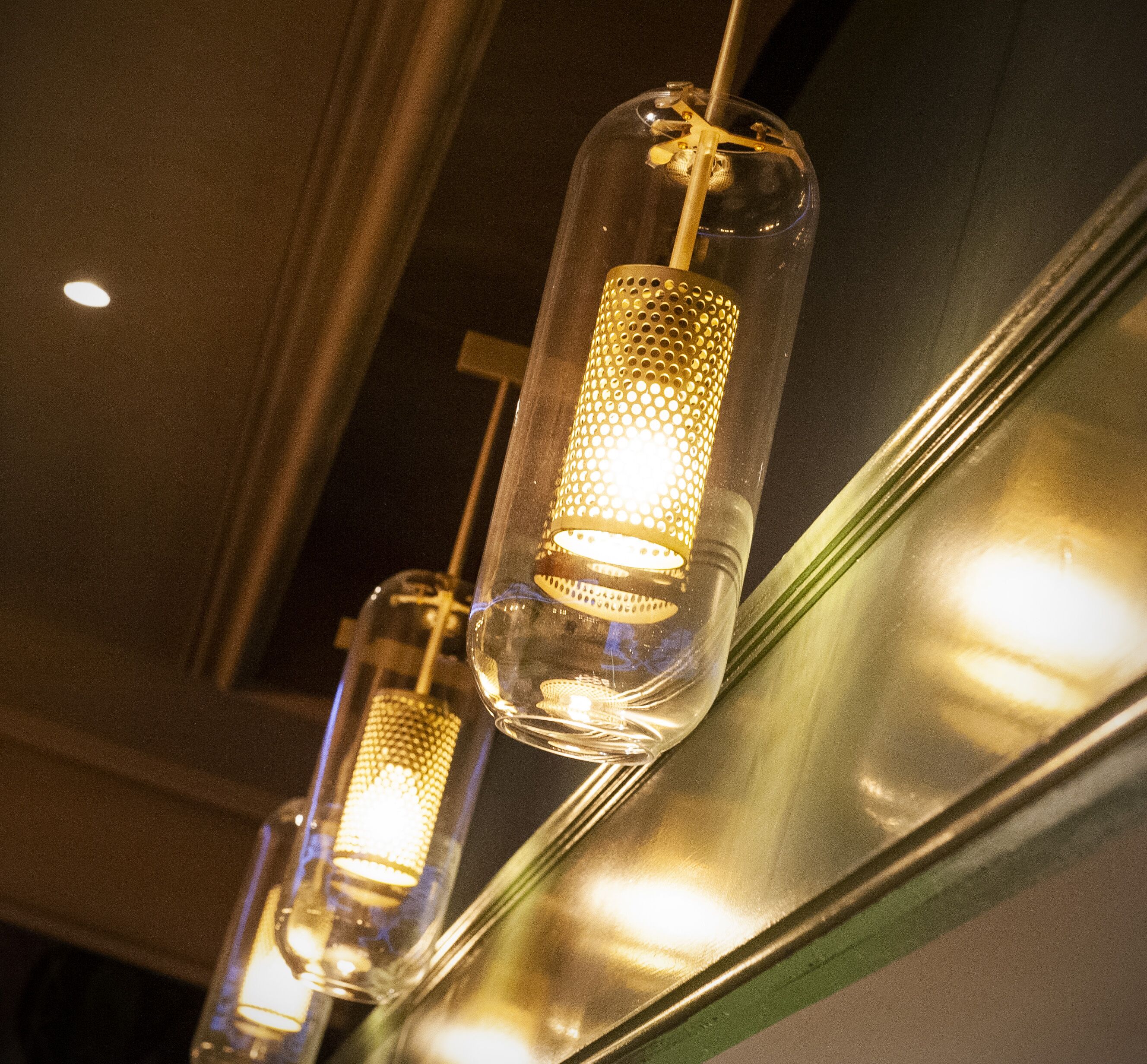 A row of hanging pendant lights with a perforated metal shade, suspended from a ceiling.