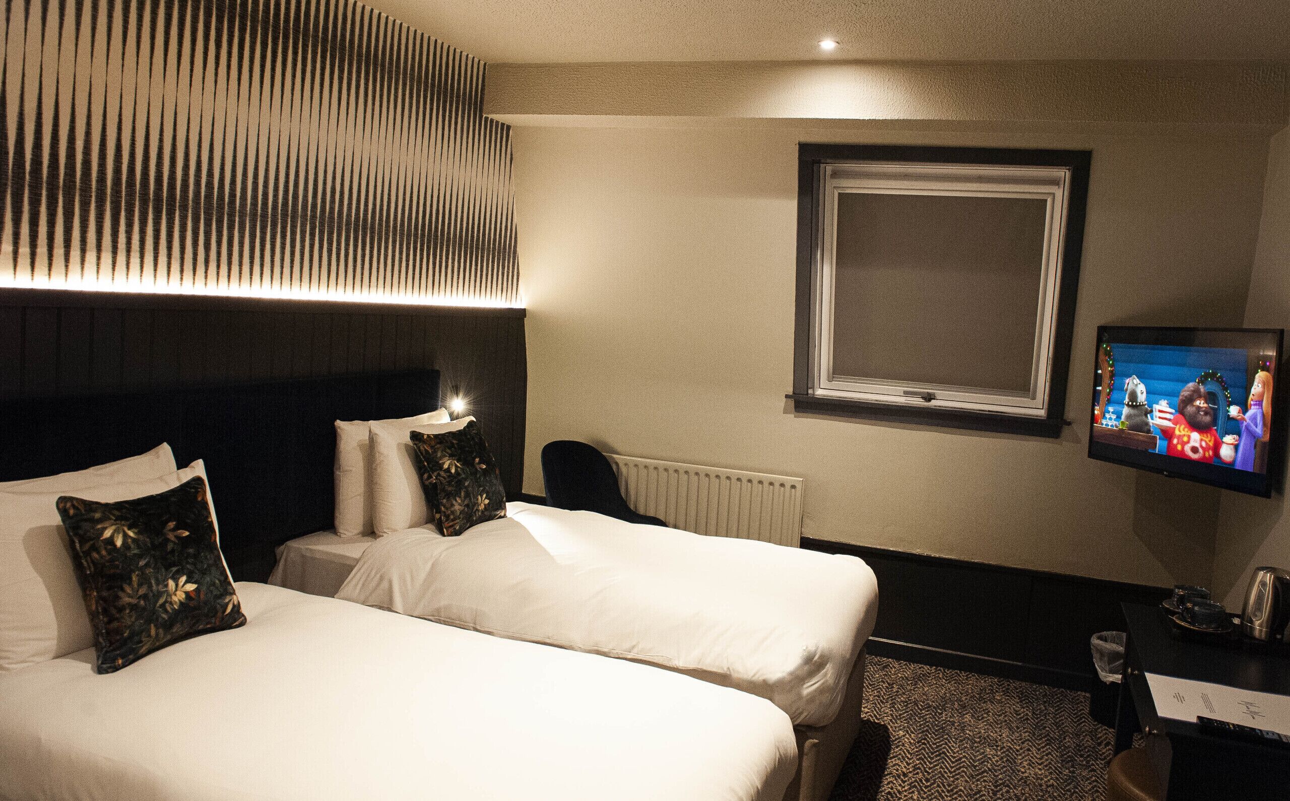 A hotel room with two beds, a television, and a window.