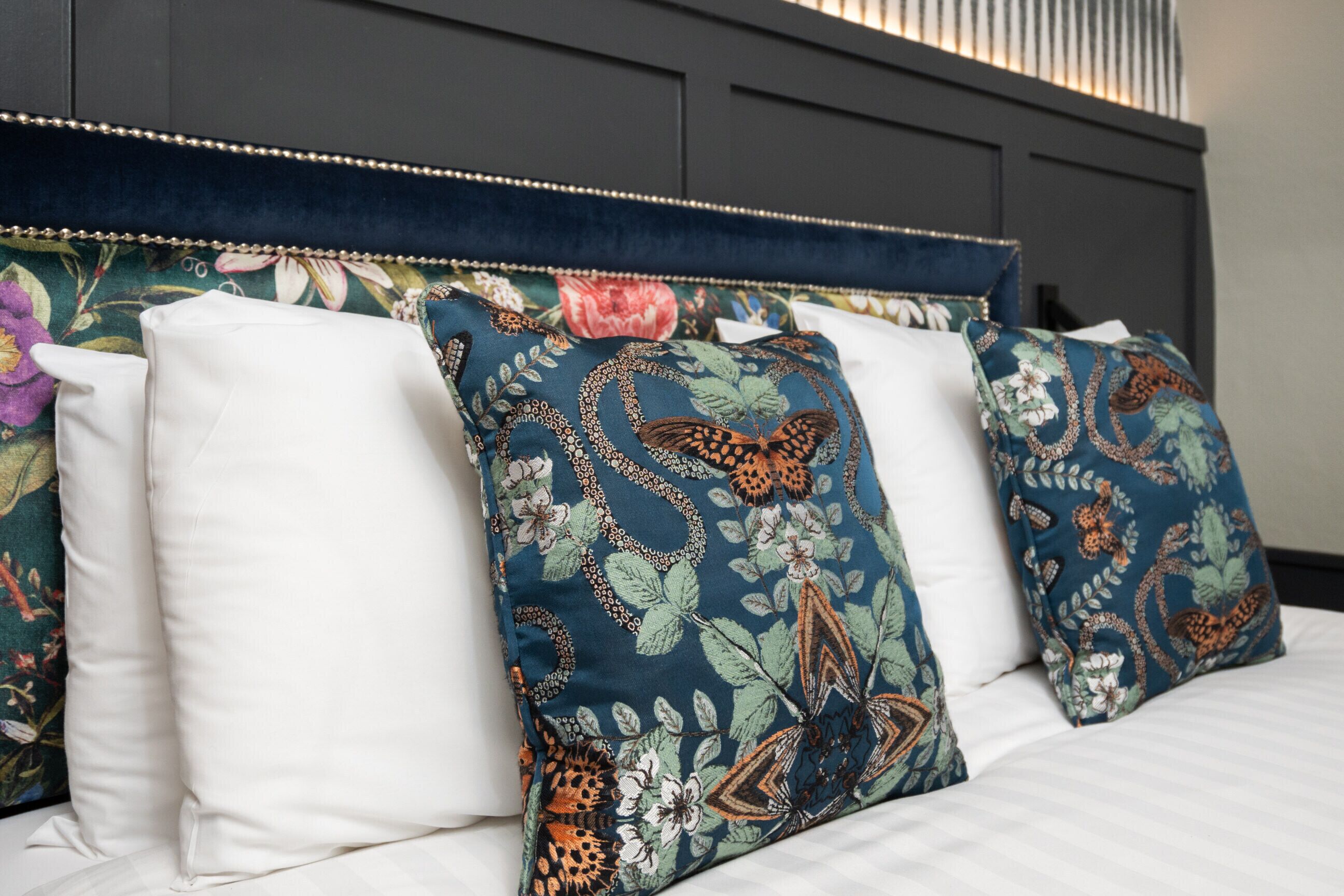 A bed with white linens and decorative pillows with floral patterns.