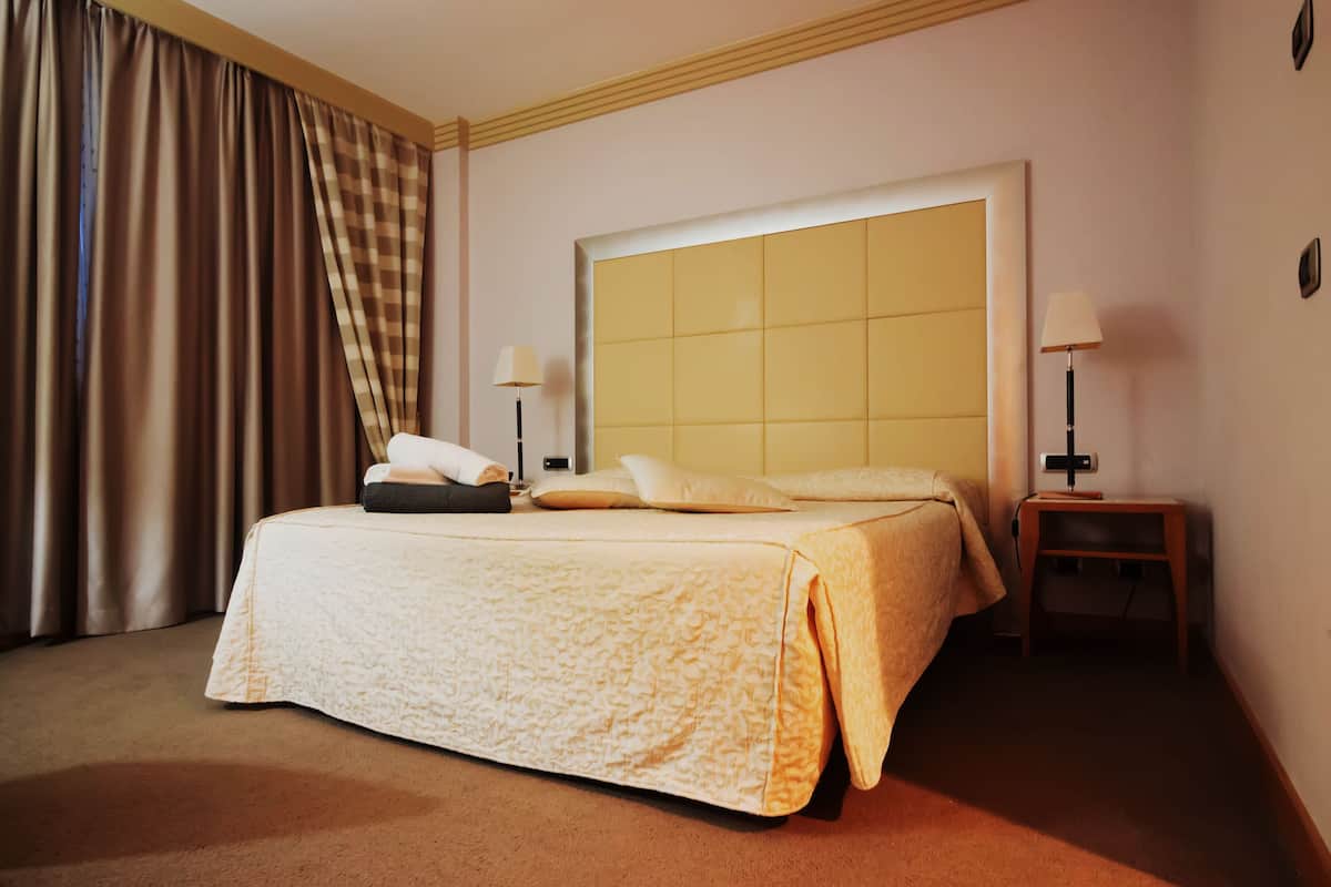 A hotel room with a large bed, two bedside tables with lamps, a checkered curtain, and a plain wall.