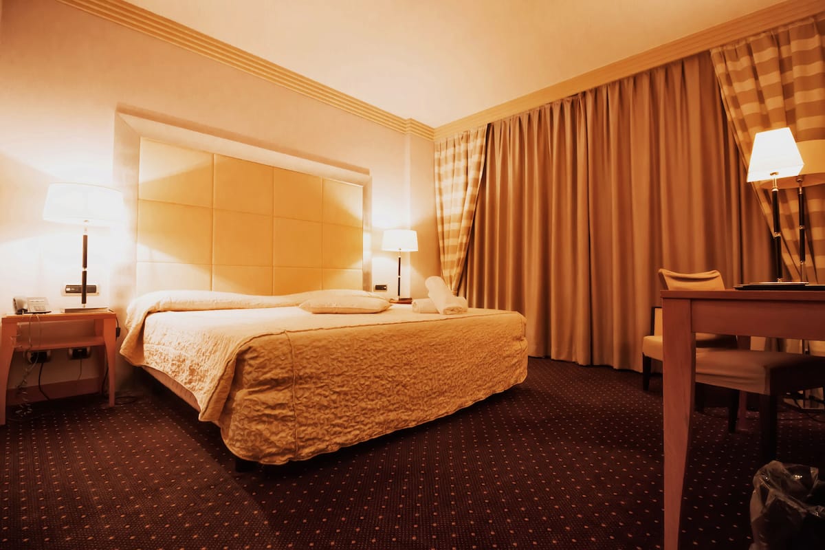 A hotel room with a large bed, two bedside tables with lamps, a small desk, and a chair.