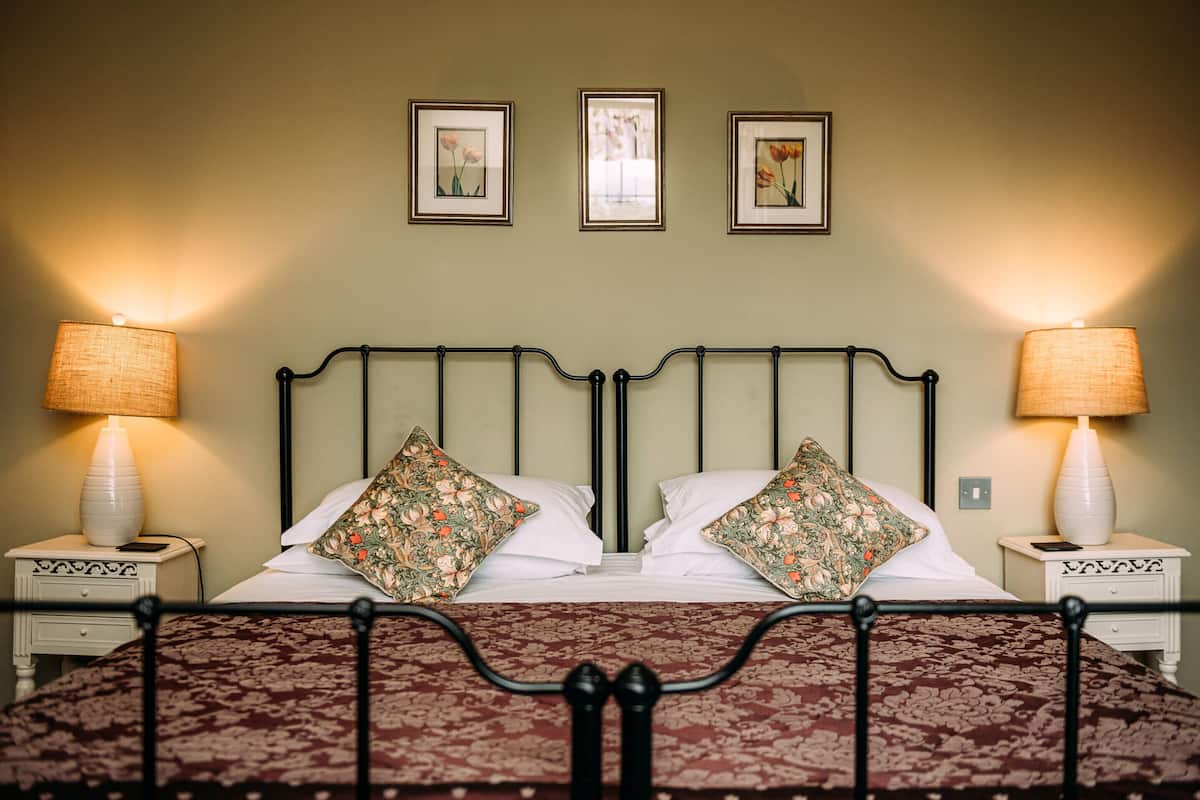 A double bed with floral pillows, two bedside lamps, and framed pictures on the wall.