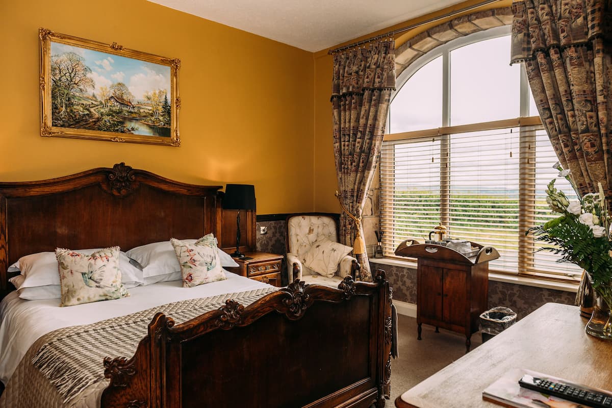 A bedroom with a large bed, a chair, a desk, and a window with curtains.