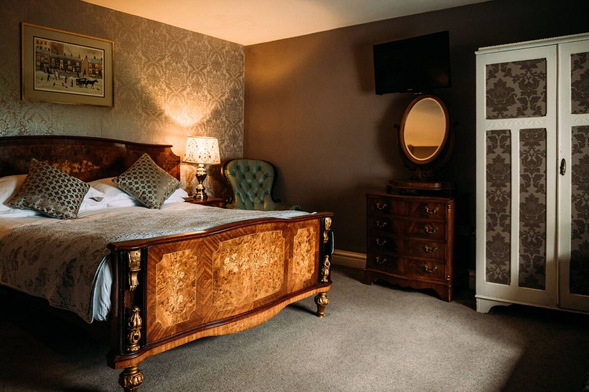 A bedroom with a wooden bed, a dresser, a mirror, and a television on the wall.