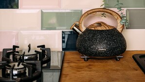 A kitchen with a gas stove, hanging pots, a hanging plant, and a decorative wooden bowl on the counter. - The Red Pump Inn (Clitheroe)