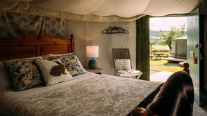 A bedroom with a large bed, a wooden headboard, a nightstand with a lamp, a chair, and a view of the outdoors through an open door. - The Red Pump Inn (Clitheroe)