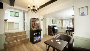 Una habitación acogedora con una escalera, una chimenea, una mesa con sillas y una máquina recreativa antigua.