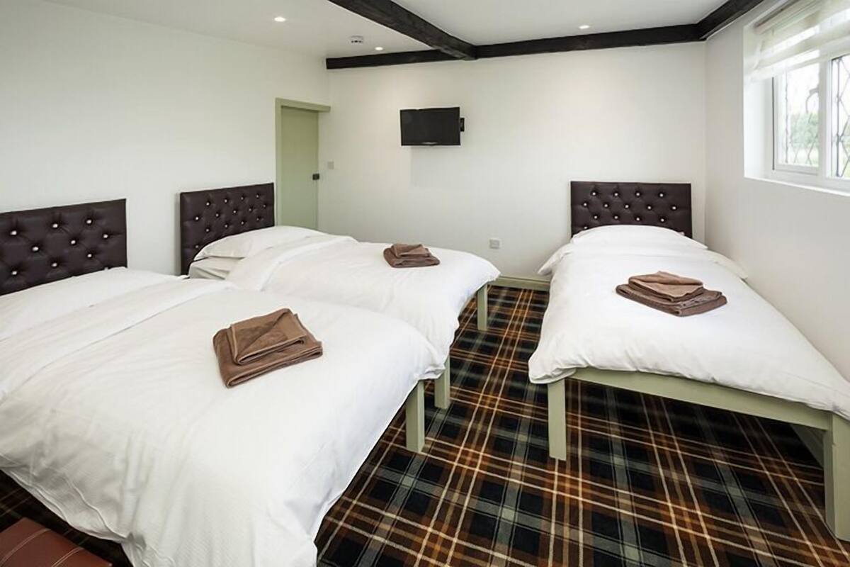 A hotel room with two beds, each with a headboard and a flat-screen TV mounted on the wall.