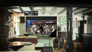 Zona de bar con una televisión mostrando un evento deportivo, muebles de madera y un letrero que dice
