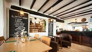 Un restaurante con una mesa y sillas de madera, un menú en una pizarra y un área de cocina al fondo.