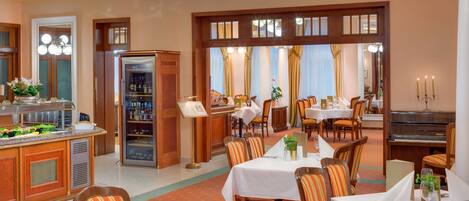 Uma área de refeições de hotel com mesas, cadeiras, um piano e um buffet.