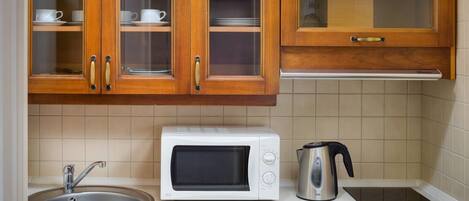 Una cocina con armarios de madera, un microondas blanco, una tetera y un lavamanos.