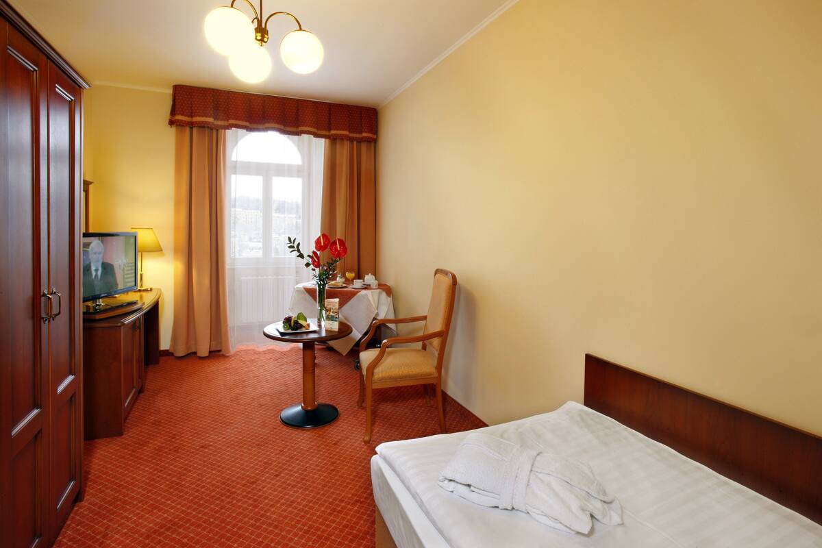 A hotel room with a bed, a desk with a chair, a television, and a window with curtains.
