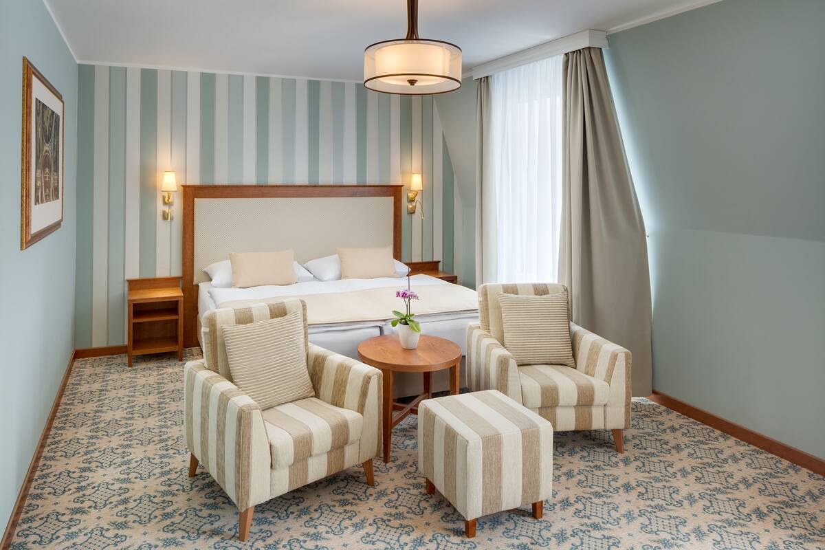 A hotel room with a bed, two armchairs, a small table, and a nightstand.
