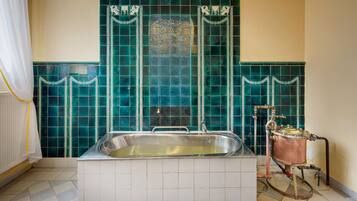 A bathroom with a bathtub, a tiled wall with a decorative pattern, and a copper water heater.